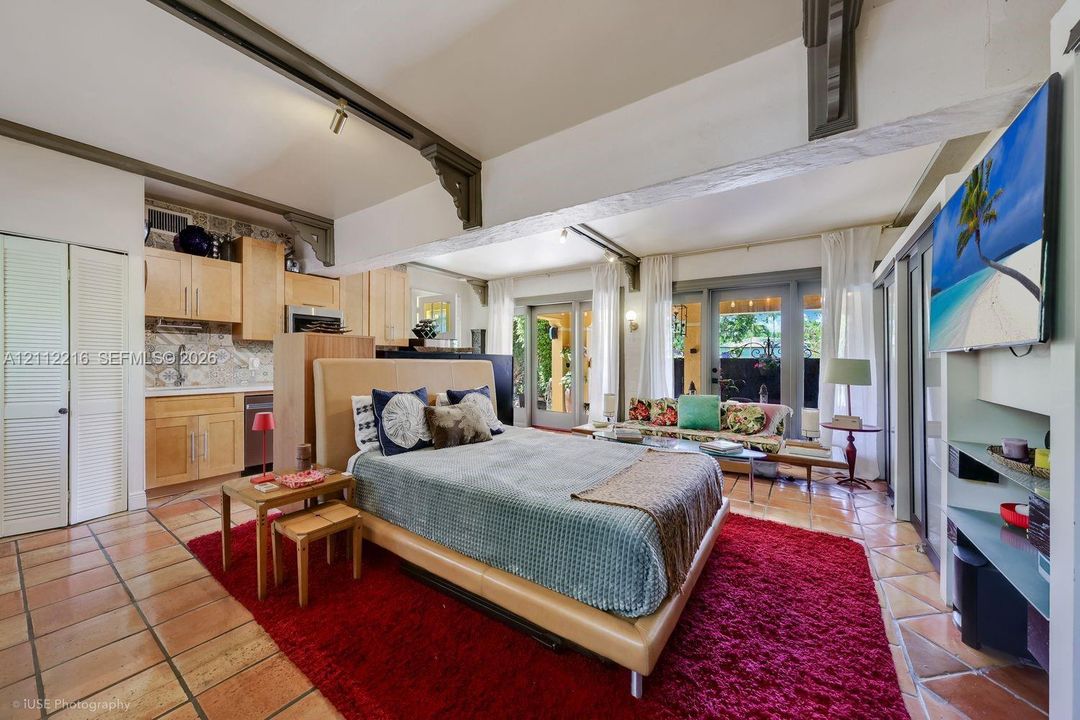Open-concept living space featuring terracotta tile flooring, exposed structural beams with decorative corbels, natural wood cabinetry, patterned tile backsplash, and dual glass-paneled exterior doors