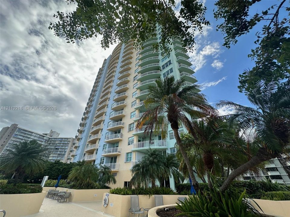 High-rise architectural exterior featuring tiered balconies, a smooth stucco facade, and an integrated paved pool deck with mature landscaping