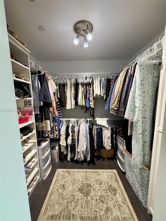 Walk-in closet featuring built-in vertical shelving, tiered hanging rods, and dark tile flooring with a brushed-nickel triple-light fixture