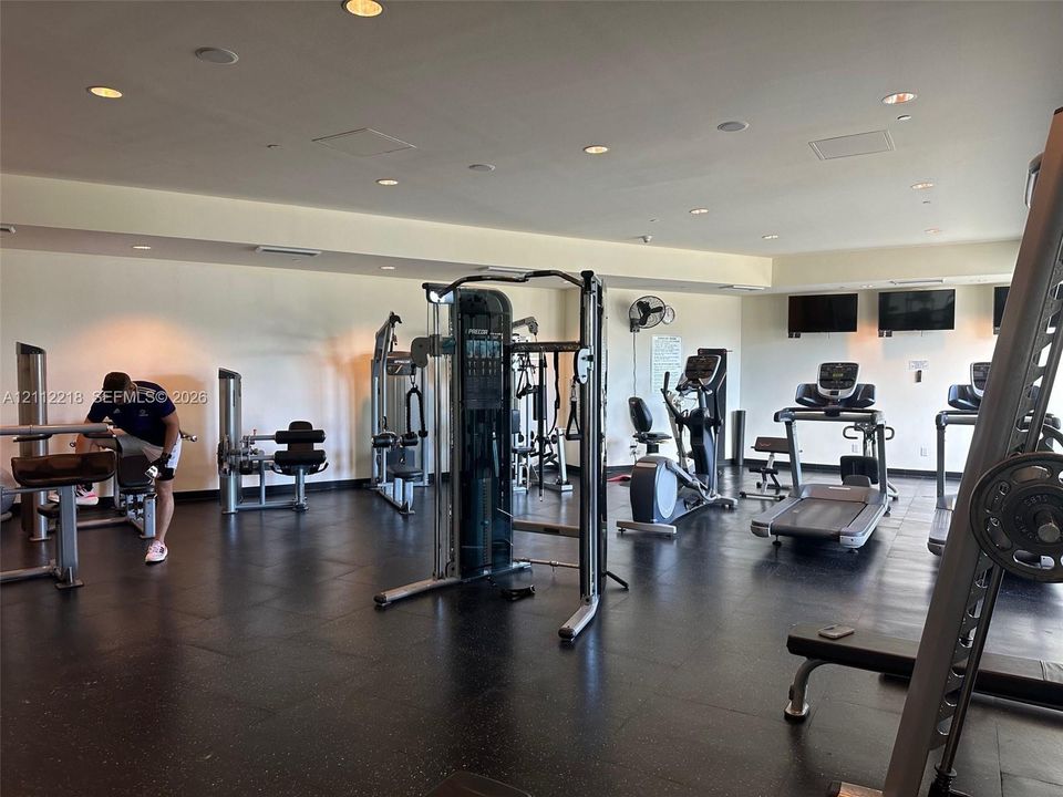 Fitness center featuring recessed lighting, dark composite flooring, and wall-mounted television screens