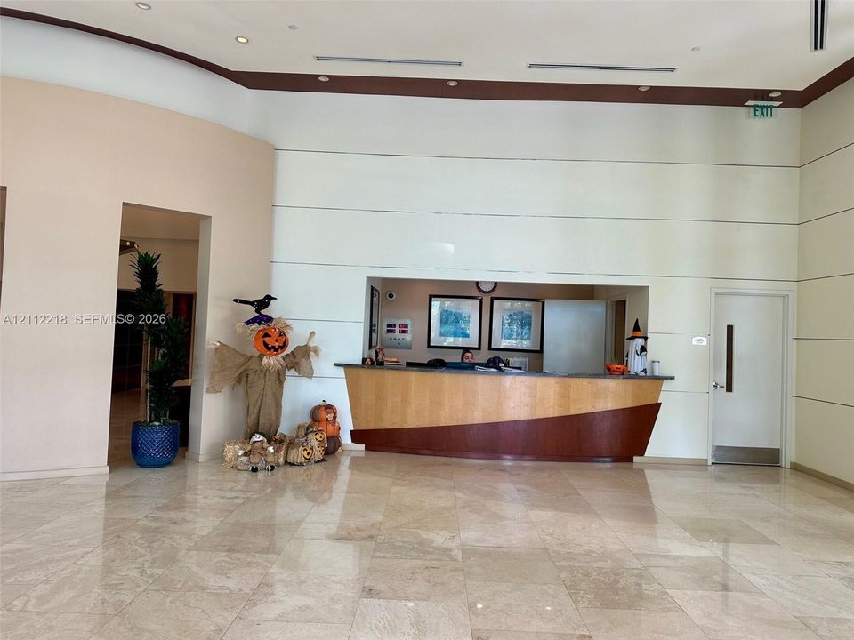 Grand lobby featuring high ceilings, polished stone flooring, recessed lighting, and a built-in reception desk with tiered wood-finish detailing
