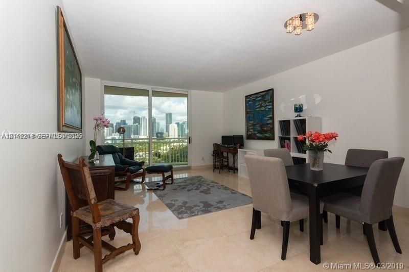 Open-concept interior featuring light-toned tile flooring, floor-to-ceiling sliding glass doors, a metal-railed balcony, and a multi-bulb flush-mount ceiling fixture