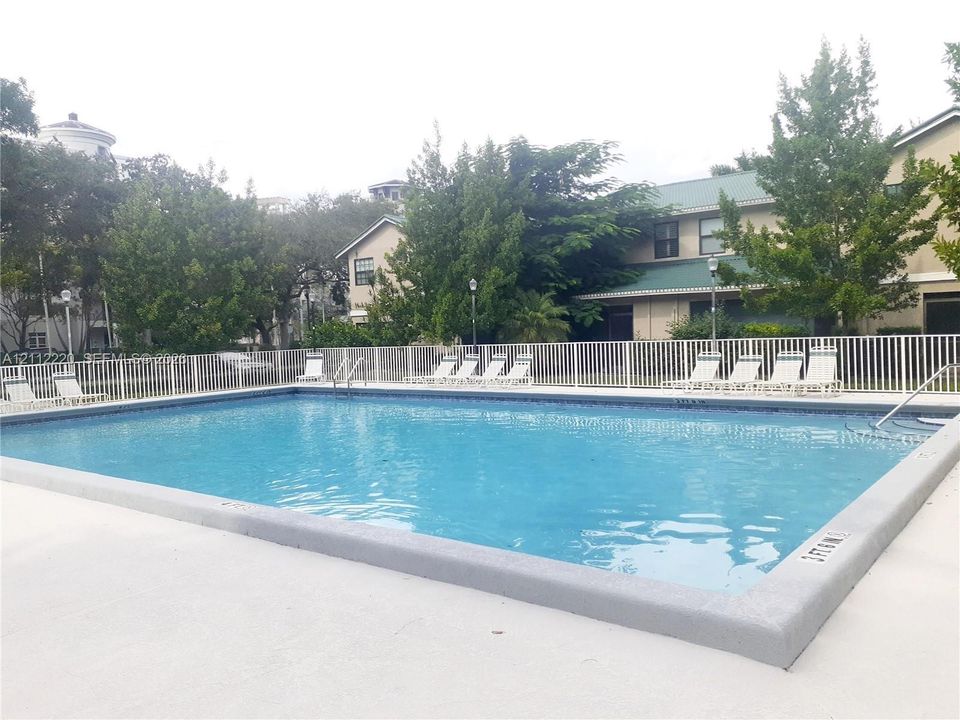 Rectangular swimming pool featuring a concrete deck, white perimeter fencing, metal ladder access, and integrated depth markers