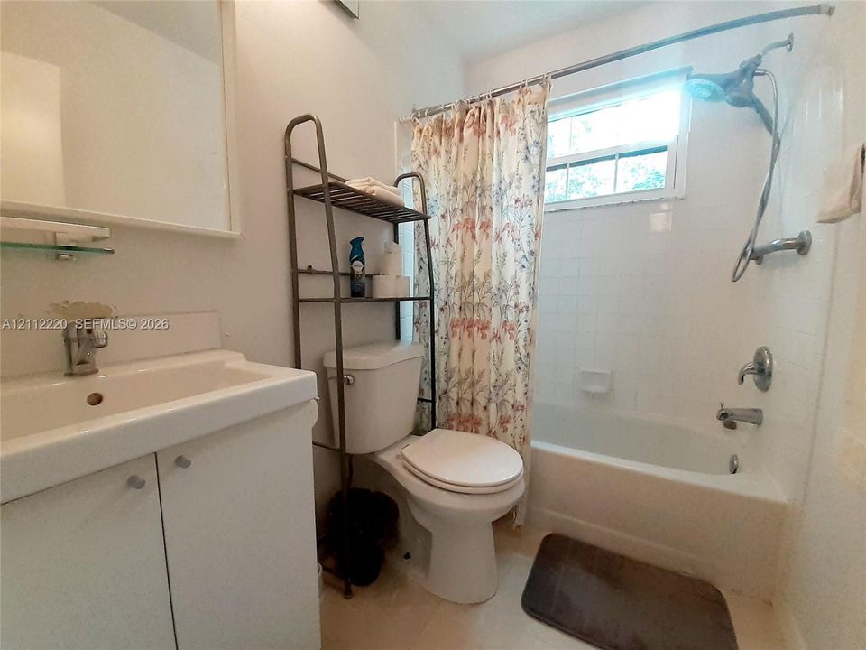 Bathroom featuring a vanity with an integrated sink, polished chrome faucet, white tiled shower surround, and a single-handle shower system