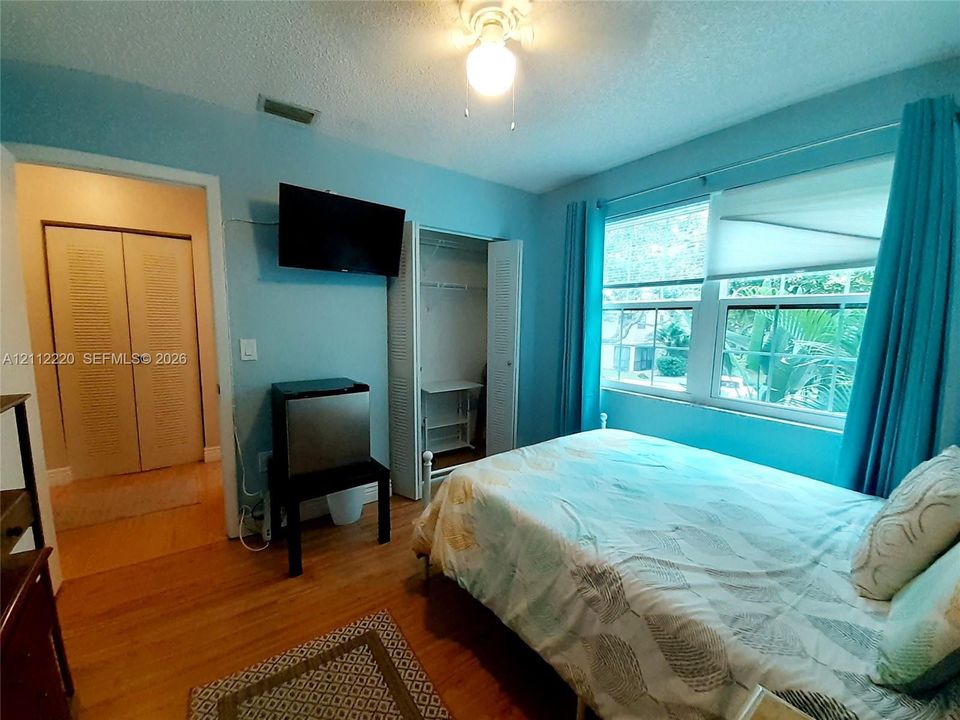 Room featuring wood-finish flooring, dual bi-fold closet doors, a multi-pane window, and a ceiling-mounted light fixture