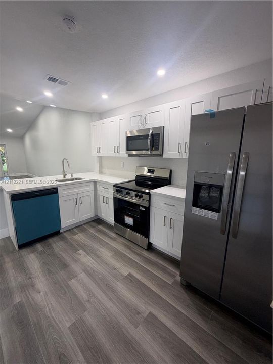 Kitchen featuring white shaker-style cabinetry, solid-surface countertops, wood-finish flooring, and stainless steel appliances