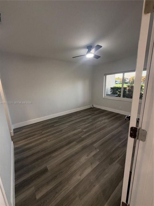 Neutral interior space featuring wood-finish flooring, a ceiling fan with integrated lighting, and a large window