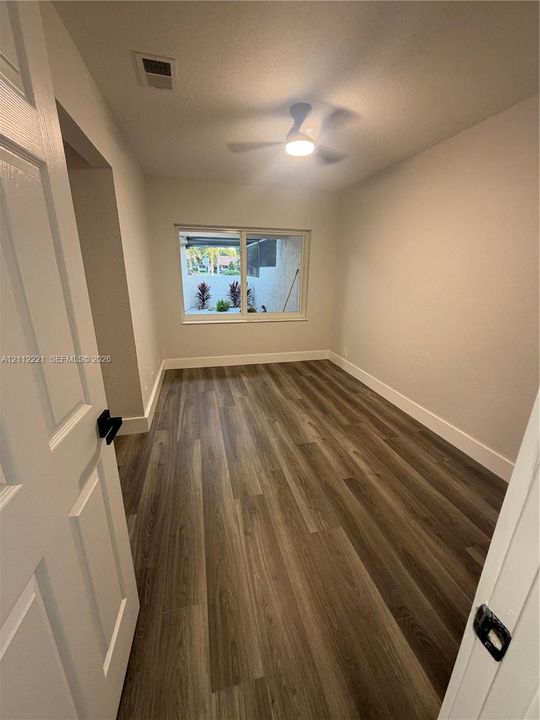 Neutral-toned interior featuring wood-finish flooring, a sliding window with exterior hardscaping, and a ceiling-mounted light fixture
