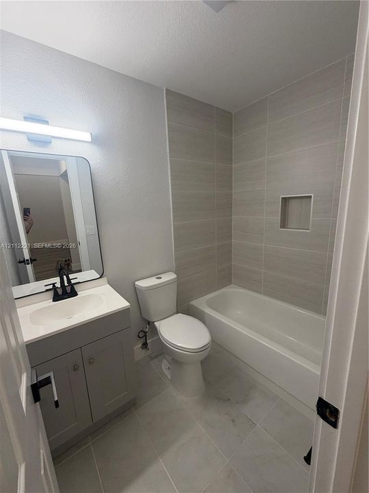 Bathroom featuring a gray shaker-style vanity with a white countertop, rectangular vessel sink with matte black faucet, wall-mounted mirror, and a tub-shower combination with floor-to-ceiling tile surround and built-in recessed shelving