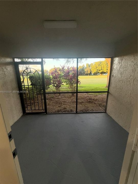 Screen-enclosed porch with textured gray concrete flooring, decorative metal security door, and exterior stucco walls