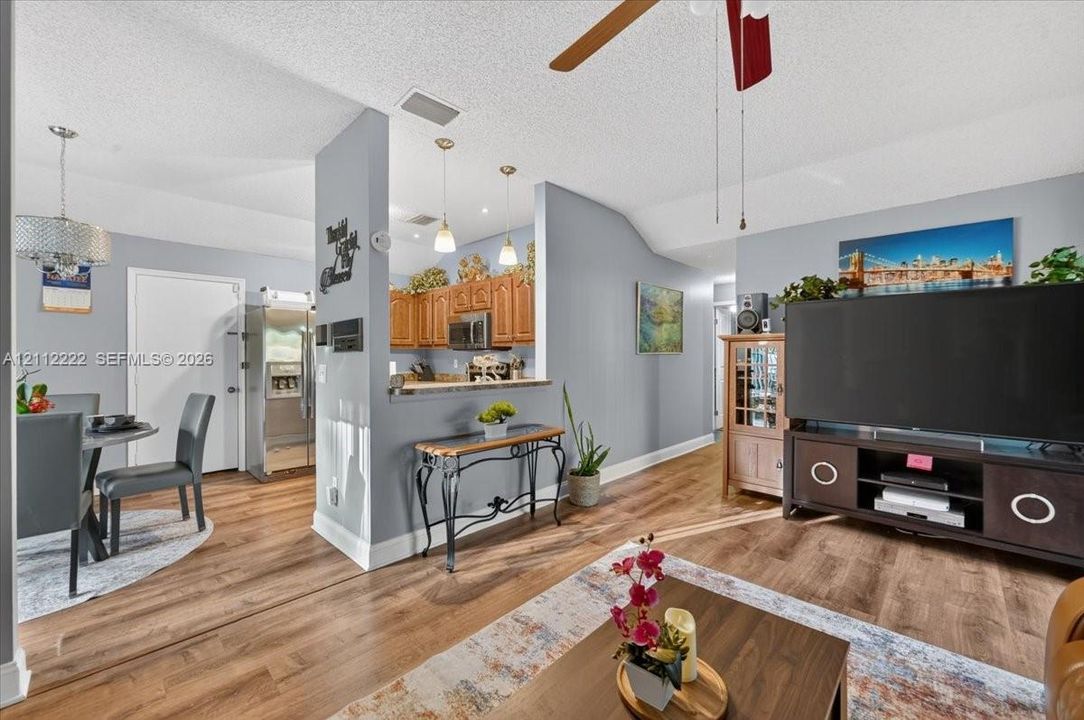 Wood-finish flooring, pass-through breakfast bar, wood cabinetry, pendant lighting, and vaulted ceilings