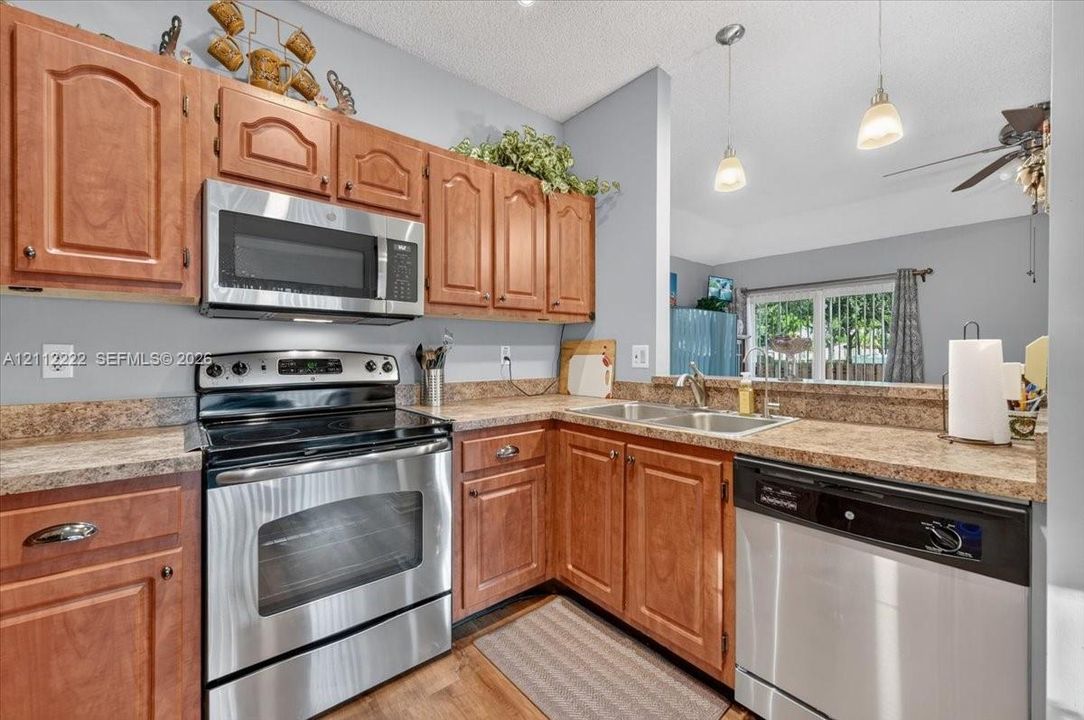 Kitchen featuring wood cabinetry, stone-finish countertops, stainless steel appliances, and dual pendant lighting