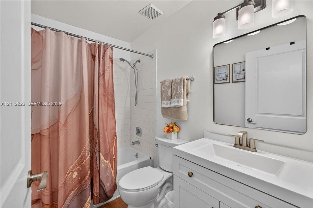 Bathroom featuring a white vanity with an integrated rectangular sink, a rectangular mirror with rounded corners, a three-light fixture, and a tub-shower combination with white subway-style wall tiling