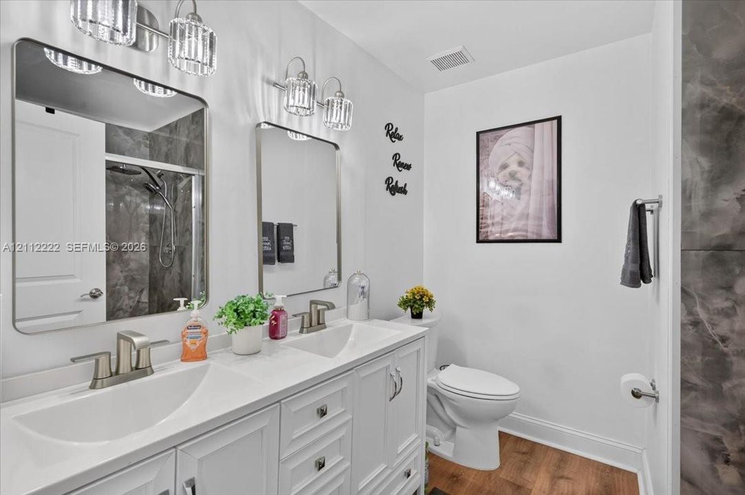 Double vanity featuring white cabinetry, a solid surface countertop with integrated dual sinks, brushed nickel fixtures, rectangular mirrors, and glass-shade wall lighting