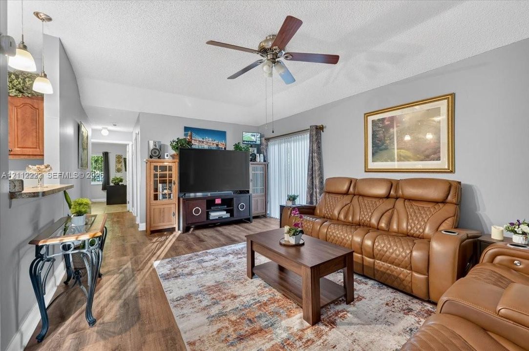 Living area featuring wood-finish flooring, vaulted ceilings, a ceiling fan, and sliding glass doors