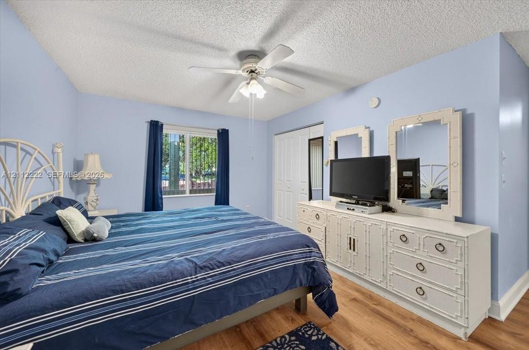 Wood-finish flooring, ceiling fan with integrated light fixture, dual-panel sliding closet doors, and multi-pane window