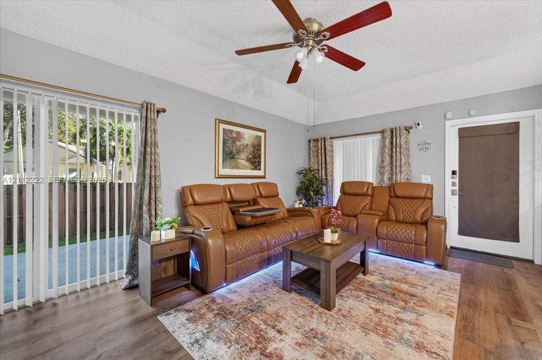 High-vaulted ceilings featuring a polished metal and wood-blade ceiling fan, sliding glass doors providing outdoor access, and wood-finish flooring