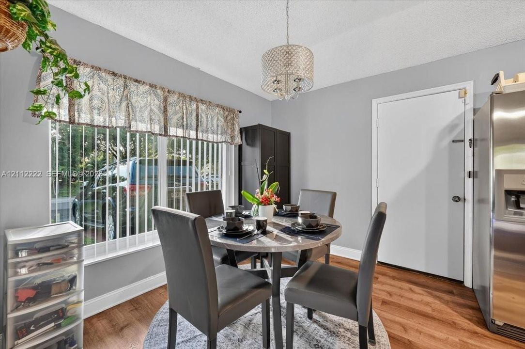 Dining area featuring wood-finish flooring, a decorative drum-style chandelier, and a large window with vertical blinds