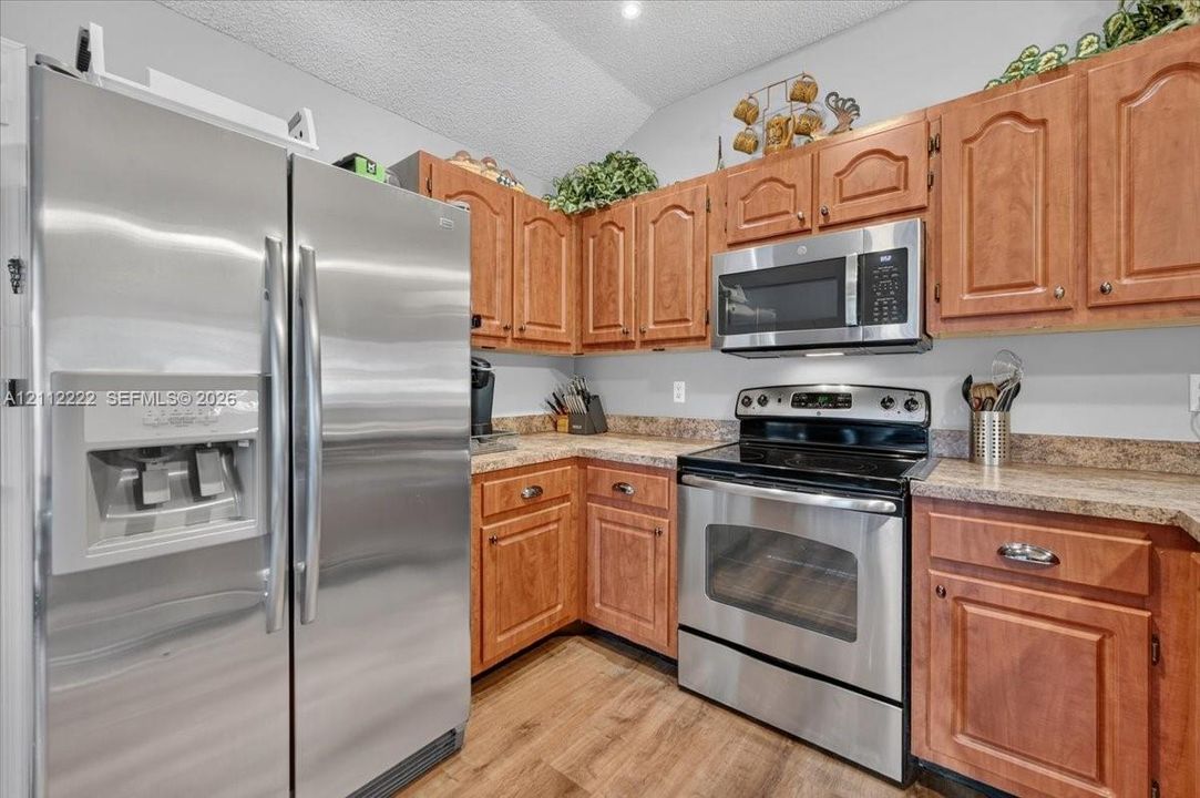Kitchen featuring wood cabinetry, stainless steel side-by-side refrigerator, matching range, over-the-range microwave, and laminate countertops with wood-finish flooring