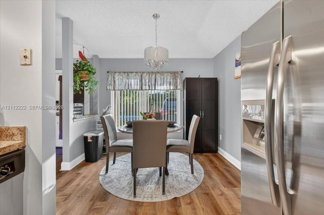 Dining area featuring wood-finish flooring, a contemporary drum pendant light fixture, and vertical window blinds