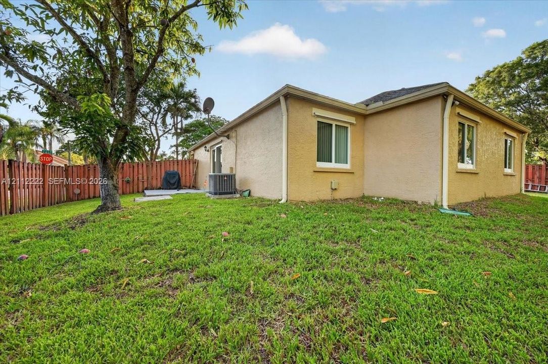 Stucco exterior residence featuring a grass lawn, mature tree, and wood-slat perimeter fencing