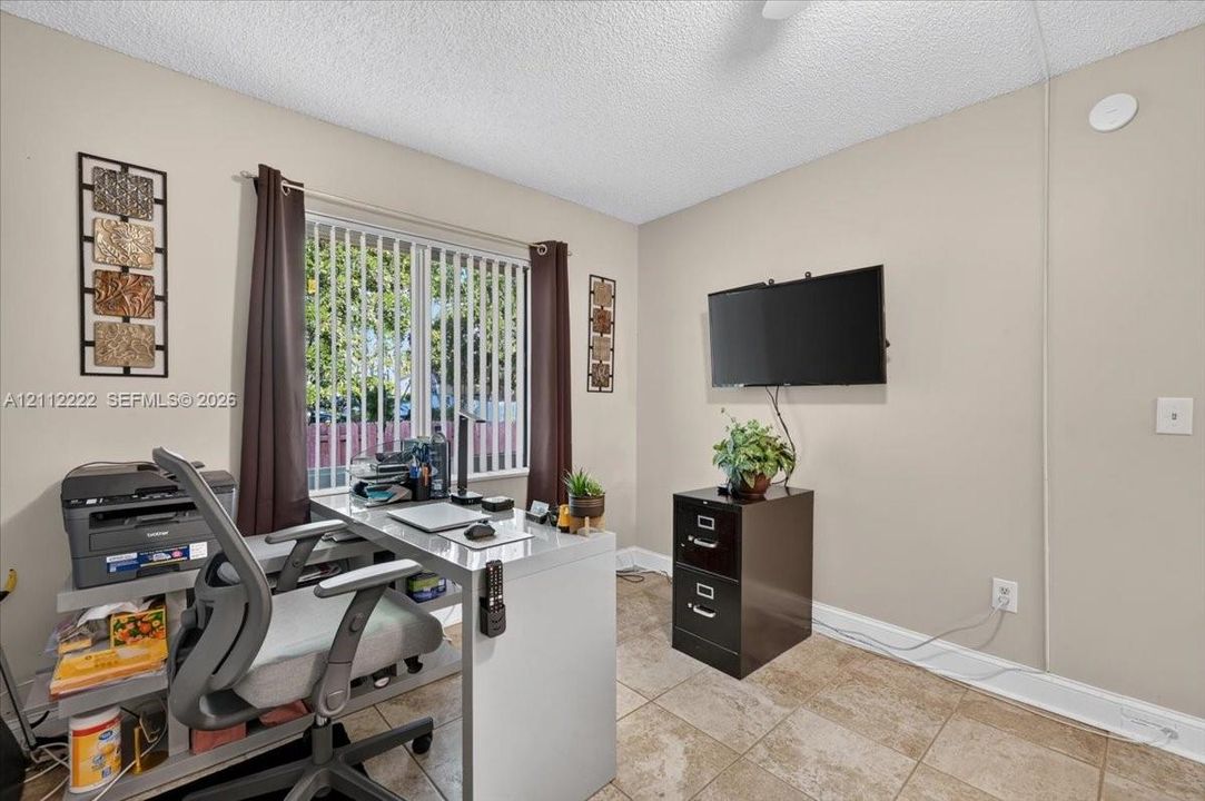 Neutral-toned interior space featuring light-colored tile flooring, textured ceiling finish, and vertical blinds
