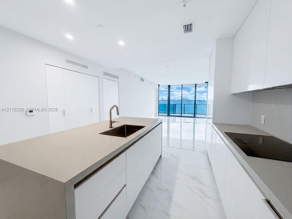 Modern kitchen featuring a central island with a waterfall-edge countertop, gloss-finish cabinetry, an integrated cooktop, and floor-to-ceiling windows