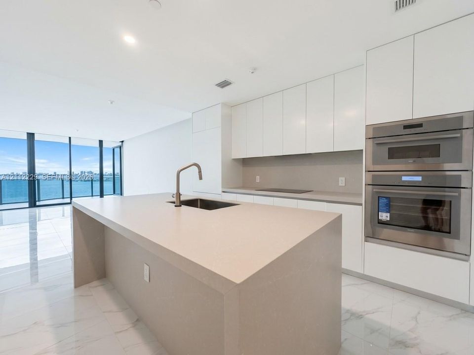 Modern kitchen featuring white flat-panel cabinetry, a central island with a solid-surface countertop, stainless steel double wall ovens, and porcelain flooring throughout