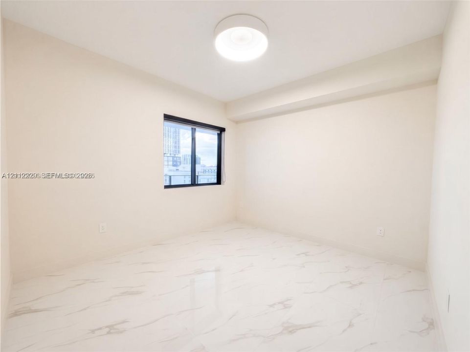 Neutral-toned interior featuring stone-finish tile flooring, recessed window casing with dark framing, and a central circular flush-mount ceiling light fixture
