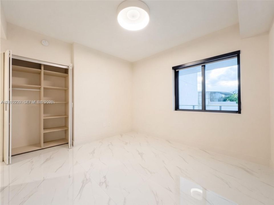 Interior space featuring polished stone-finish flooring, a built-in closet with integrated shelving, a modern flush-mount ceiling light, and a black-framed window
