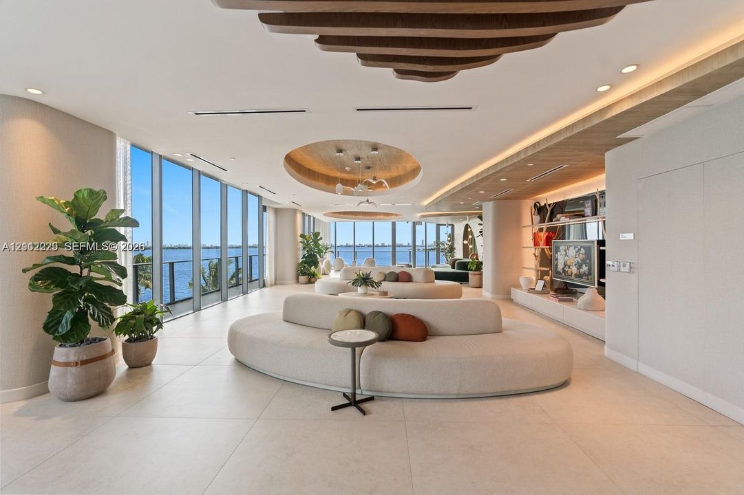 Open-concept living space featuring floor-to-ceiling windows, large-format tile flooring, recessed circular ceiling treatments with integrated lighting, and custom built-in wood-finish shelving