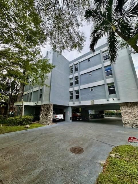 Multi-story residential building featuring a concrete facade, stone-clad structural pillars, and a ground-level parking area