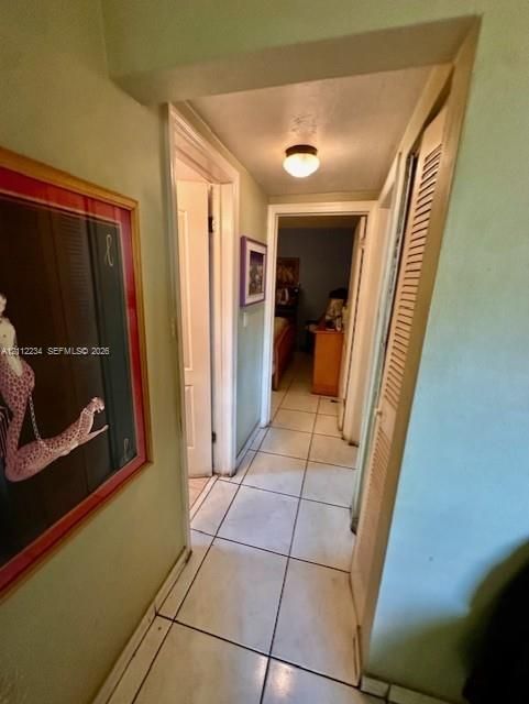 Hallway featuring neutral-toned tile flooring, flush-mount lighting, and louvered closet doors