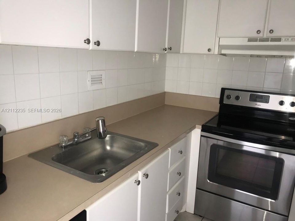 Kitchen featuring white cabinetry, solid surface countertops, stainless steel electric range, square-tile backsplash, and drop-in sink with dual-handle faucet