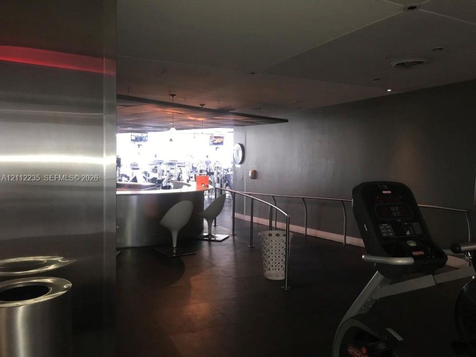 Fitness area featuring dark tile flooring, a curved stainless steel bar, recessed ceiling lighting, and metal handrails