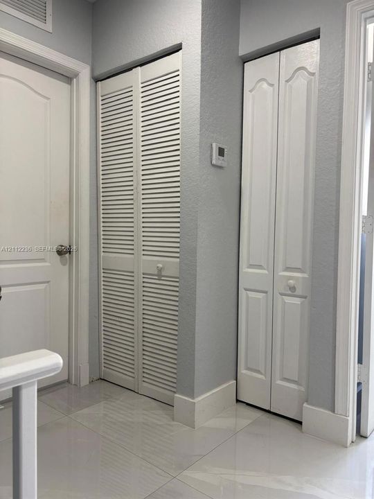 Neutral interior featuring large-format ceramic tile flooring, white six-panel door, louvered double-door storage, and a paneled bifold door