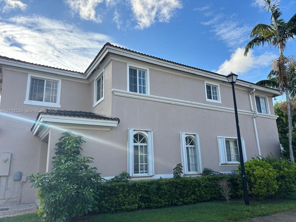 Two-story stucco exterior featuring arched windows, multi-pane glass, tiled roofline, and manicured landscaping