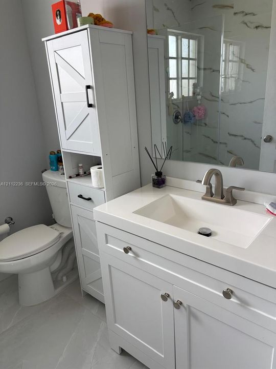 Bathroom featuring a white vanity with an integrated basin, quartz-style countertop, tall built-in storage cabinetry with matte black hardware, and large-format tile flooring
