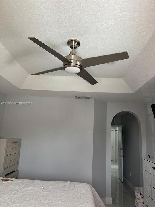 Tray ceiling featuring a brushed nickel four-blade ceiling fan with an integrated light fixture and a structural arched doorway