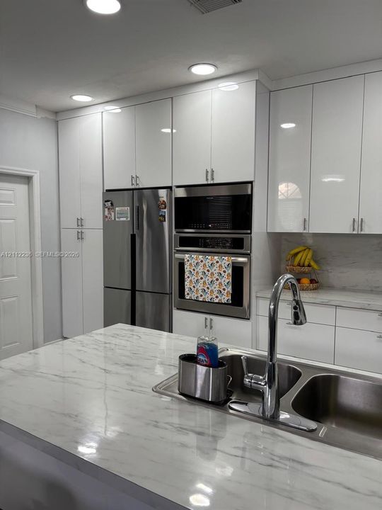 Kitchen featuring high-gloss white cabinetry, stone-finish countertops, stainless steel appliances, built-in double wall ovens, and a double-basin undermount sink with a gooseneck faucet