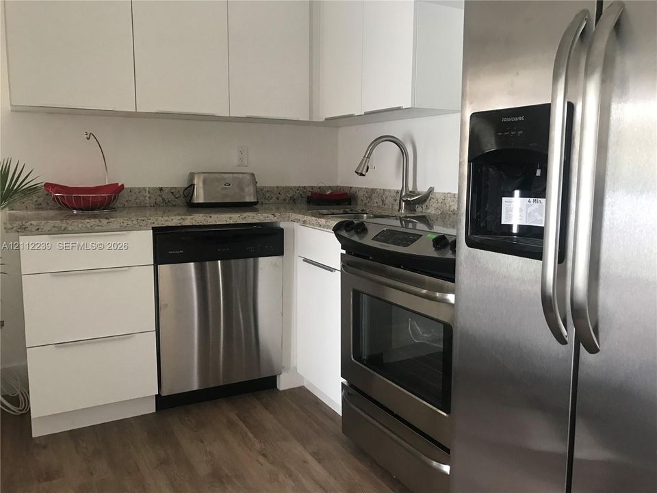 Kitchen featuring white flat-panel cabinetry, stone countertops, stainless steel appliances, and wood-finish flooring