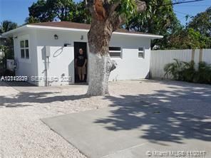Single-story exterior featuring white stucco siding, a concrete parking pad, gravel ground cover, and a white privacy fence