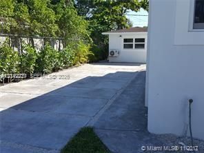Concrete driveway, white stucco exterior, detached structure with window, and chain-link perimeter fencing