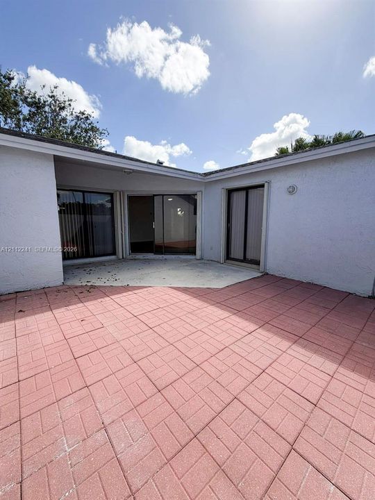 Enclosed courtyard featuring brick-patterned pavers and multiple sliding glass door entries