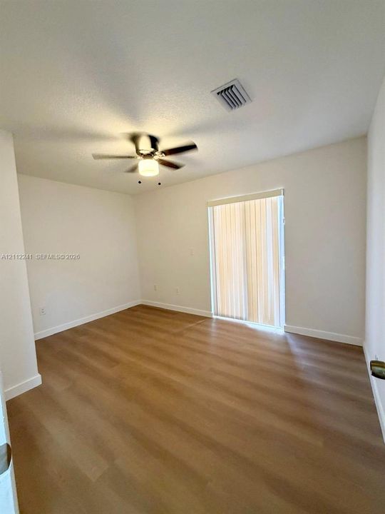 Room featuring wood-finish flooring, a ceiling fan with integrated lighting, and a sliding glass door with vertical blinds