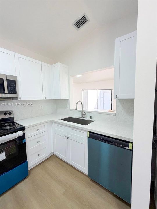 Kitchen featuring white shaker-style cabinetry, solid-surface countertops, a stainless steel undermount sink with a gooseneck faucet, and stainless steel appliances