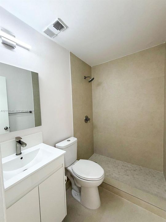 Bathroom featuring a white vanity cabinet with a stone-top integrated sink, a rectangular frameless mirror, and a walk-in shower with neutral tile surround and stone mosaic flooring