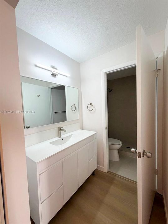 Bathroom featuring a white vanity with an integrated sink, polished chrome faucet, large rectangular mirror, and light-tone wood-finish flooring