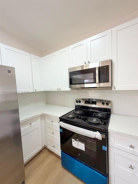 White Shaker-style cabinetry, solid-surface countertops, stainless steel refrigerator, built-in microwave, and electric range