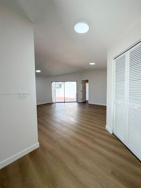 Interior space featuring wood-finish flooring, white walls, louvered-style closet doors, recessed ceiling lighting, and sliding glass doors